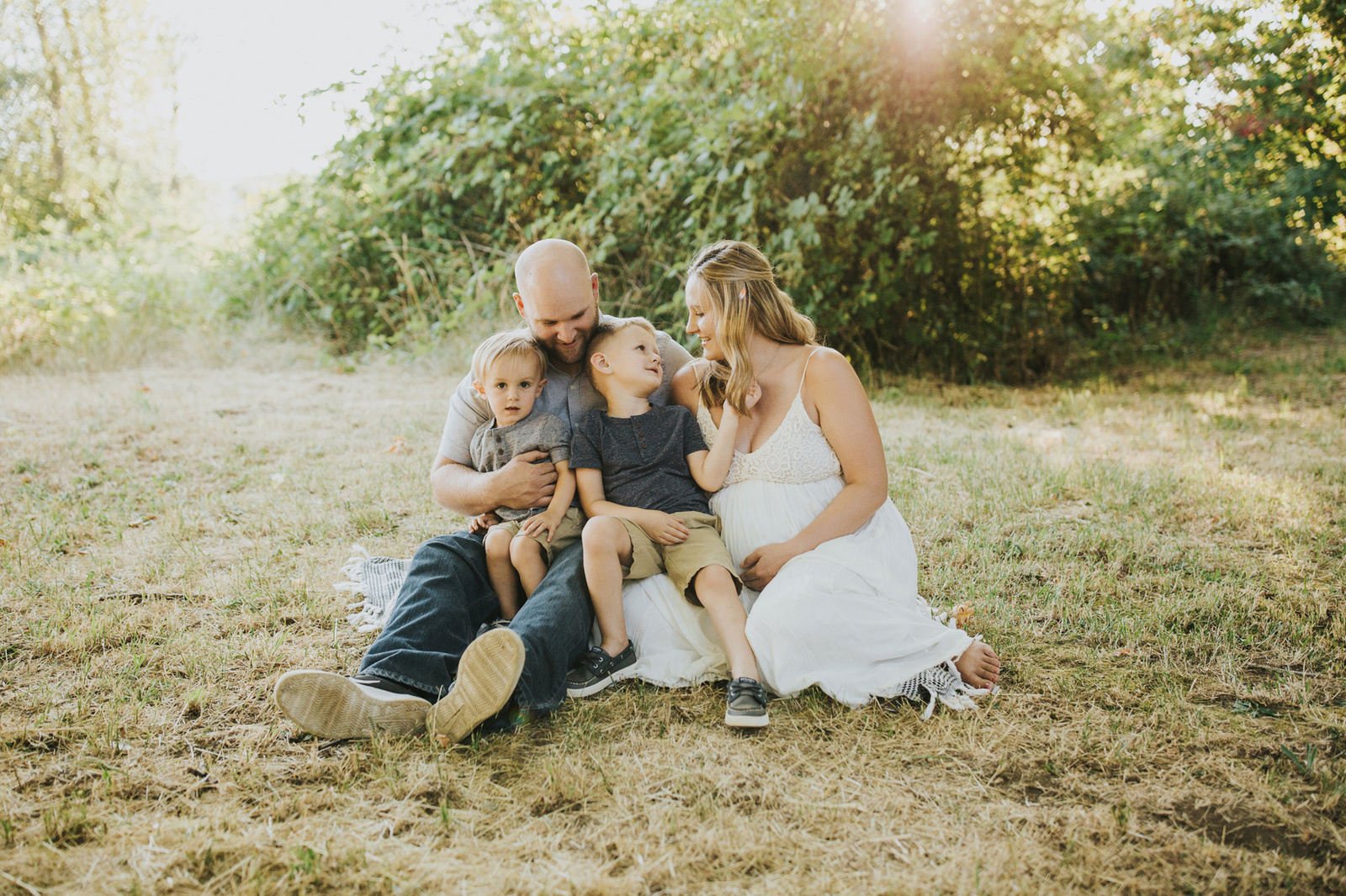 Family of four, including an expectant mom, snuggle on a blanket on the ground during a Yamhill, OR maternity session.